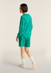 Conjunto de sudadera y pantalones cortos en color turquesa que presenta un patrón texturizado, cuello redondo, mangas largas y puños acanalados, combinado con calcetines y zapatos blancos.