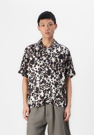 Camisa de manga corta con estampado de leopardo en tonalidades de marrón y negro sobre un fondo blanco, con un cuello clásico y diseño de botones en la parte delantera.