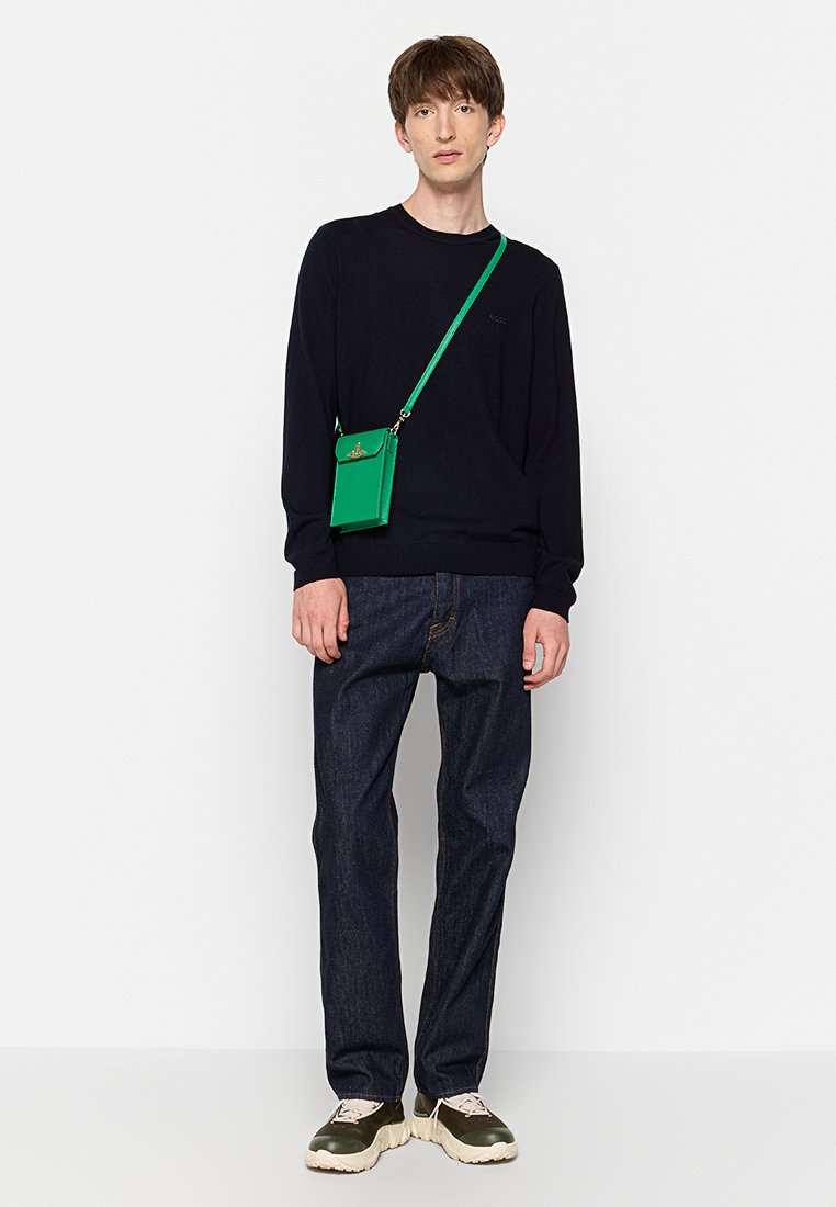 Groene schoudertas met gouden hardware, marineblauwe trui, donkere spijkerbroek en chunky sneakers met een crème en olijf kleurenschema.