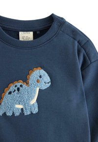 Marineblaues Sweatshirt aus weicher Baumwolle mit einer strukturierten blauen Dinosaurier-Applikation, die braune und schwarze Akzente aufweist. Druckknöpfe an der Schulter.
