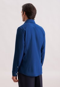 Camicia blu a maniche lunghe realizzata in tessuto testurizzato, con colletto button-down e bottoni ai polsini, caratterizzata da un orlo curvo e yoke posteriore.