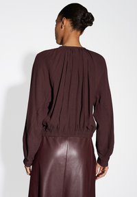 Bordeaux lichtgewicht top met lange mouwen, geplooide achterkant en gathered tailleband, gecombineerd met een bijpassende leren rok. Soepele textuur.