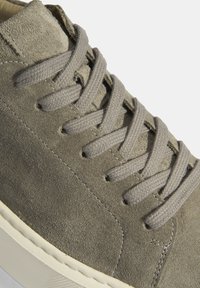 Gray suede sneaker with a smooth texture, featuring light gray laces, a rounded toe, and a white rubber sole with textured details.