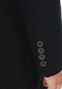 Rękaw czarnej wełnianej marynarki z czterema czarnymi guzikami oraz widocznym szyciem na mankiecie, o gładkiej fakturze.