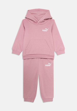 Ružový set mikiny a nohavíc vyrobený z mäkkej tkaniny. Obsahuje kapucňu, klokaniu kapsu a biely logotyp Puma na oboch kusoch.