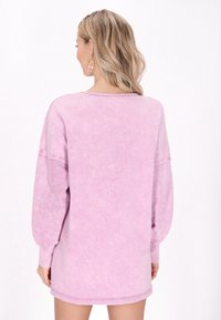 Felpa oversize rosa con maniche lunghe, una texture morbida e un aspetto sbiadito. Presenta un collo rotondo e polsini a costine.