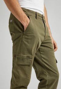 Olivgröna cargobyxor med sidofickor, tillverkade av bomullstyg. Har en rak passform och en synlig logotagg på midjebandet.