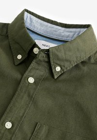 Chemise olive à col classique avec des boutons blancs et une doublure intérieure rayée bleu et blanc.