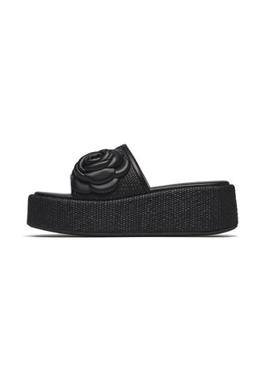 Black platform slide sandal with woven textured sole and large black leather flower embellishment on upper strap.
