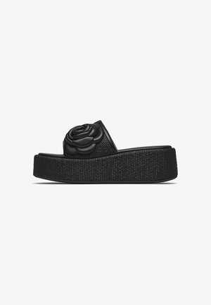 Sandalo con plateau nero, suola intrecciata e decorazione grande a fiore in pelle nera sulla fascia superiore.