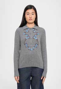 Grijze geribde trui met een kraaghalslijn, voorzien van blauwe bloemenborduursels en bruine accenten. Voorzien van knoopsluiting aan de voorkant en lange mouwen.