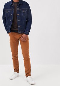 Chaqueta vaquera en azul oscuro, con dos bolsillos en el pecho y herrajes metálicos, combinada con pantalones chinos color caqui y zapatillas blancas.