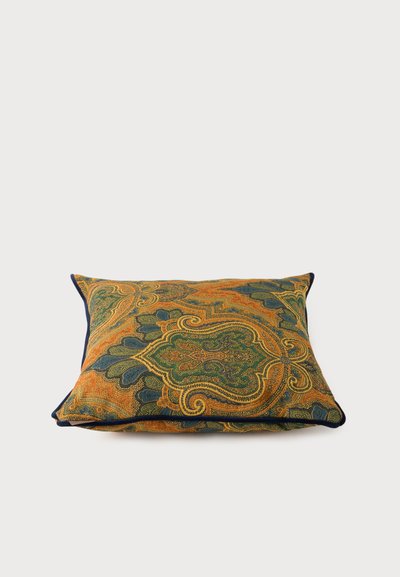 Coussin carré avec motif cachemire orné dans les tons verts, orange et bleus, doté d’un passepoil bleu foncé sur fond blanc.