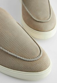 Beige slip-on cipők, textúrált felsőrésszel, gyémántmintával és kontrasztos varrással a széleken, krém színű talpon.
