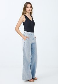 Body nero a coste abbinato a jeans a vita alta, larghi e di colore blu chiaro, con tasche laterali e una vestibilità comoda, indossato con sandali piatti.