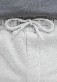 Sudadera gris con escote redondeado, combinada con pantalones de chándal gris claro que cuentan con una cintura con cordón y una tela suave y texturizada.