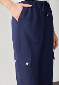 Pantaloni cargo blu navy realizzati in tessuto leggero, dotati di una vita elasticizzata, tasche laterali e dettagli con bottoni a pressione sulla tasca della coscia.