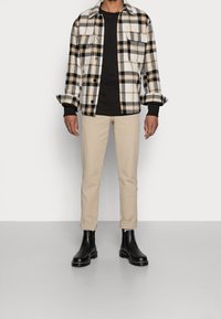 Rutig flanellskjorta i off-white, svart och orange; svart t-shirt; beige slim-fit byxor; svarta ankelboots; avslappnad look.