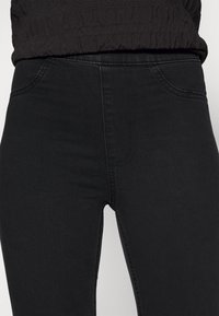Jeans de tiro alto negros con una textura suave, corte slim, con trabillas para el cinturón y un ligero estiramiento para mayor comodidad. Sin desgastes visibles ni patrones.