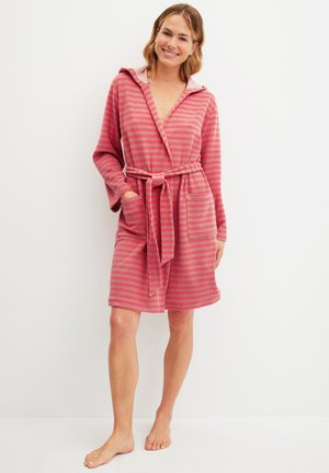 Woman smiling, standing barefoot, wearing knee-length pink and gray striped hooded robe with belt and front pockets.