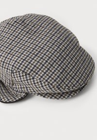 Grå og brun houndstooth-mønstret hat med en afrundet top, buet skygge og sømløs tekstur lavet af blødt stof.