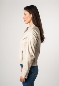 Beige leren jack met een getailleerde silhouette, ritssluiting, zijzakken en subtiele schouderaccenten, gedragen over blauwe jeans.