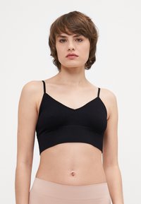 Svart ribbad crop top med tunna remmar, med V-ringning och en sömlös design. Mjuk textur med en åtsittande silhuett.