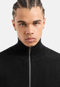 Maglione nero a coste con collo alto e zip completa, caratterizzato da un cursore in metallo argentato e un tessuto testurizzato.