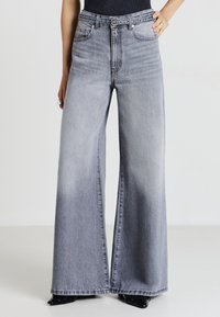 Jeans a gamba larga in denim grigio chiaro, con vita alta, design a cinque tasche e leggere sfumature. Accentati da dettagli in metallo.