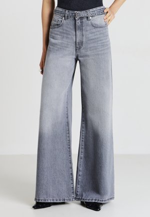 Jean large en denim gris clair, avec taille haute, design à cinq poches et décoloration subtile. Agrémenté de détails en métal.