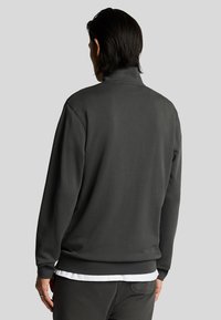 Felpa grigia scura con colletto alto, maniche lunghe e orlo a costine. Tessuto morbido, design minimal e senza motivi o accenti visibili.