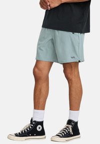 Pantalones cortos deportivos de color verde claro con una textura suave, bolsillos laterales y el logo de VA. Combinados con zapatillas altas negras y calcetines blancos.