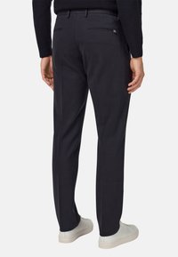 Tumši zili bikses ar gludu tekstūru, ar divām aizmugures kabatām un taisnu kāju dizainu, saskaņotas ar baltām kedām.