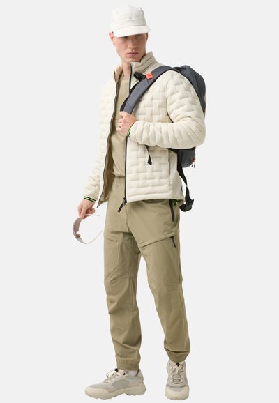 Beige puffer jacket with quilted pattern, paired with light brown cargo pants, grey backpack, and beige sneakers. Accessories include sunglasses.