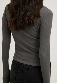 Maglione a maniche lunghe a costine di colore grigio scuro, con design aderente e texture liscia. Abbinato a pantaloni in denim neri a vita alta.