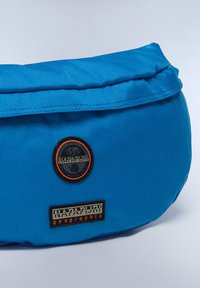 Blå tygväska med en strukturerad yta, rundad form och två broderade logotypmärken i svart och orange.