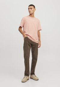 Lichtroze katoenen T-shirt met korte mouwen en een logo-opdruk, gecombineerd met bruine spijkerbroeken en beige schoenen met veters.