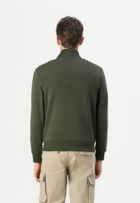 Mørkegrøn striktrøje med høj krave, ribbede manchetter og kant, parret med beige cargo-bukser, der viser et enkelt, afslappet design.