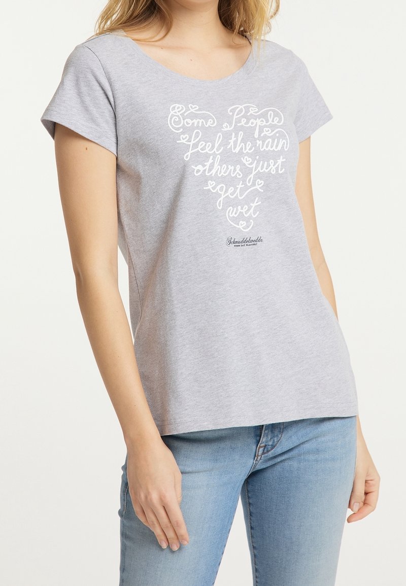 T-shirt gris à manches courtes en coton. Présente un design texte blanc avec des cœurs, indiquant : « Certaines personnes ressentent la pluie, d'autres se contentent de se mouiller. »