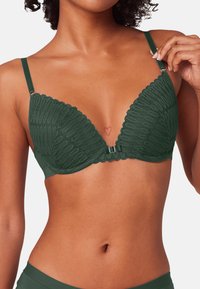 Czarny stanik z koronkowym wykończeniem, o głębokim dekolcie, z miękkiego materiału, z regulowanymi ramiączkami oraz ozdobną zapięciem z przodu. Wzory strukturalne na całej powierzchni.