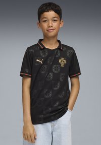 Črna nogometna majica z nevsiljivim vzorcem emblema, zlatimi poudarki, V-izrezom in črtastim ovratnikom z zelenimi in rdečimi detajli.