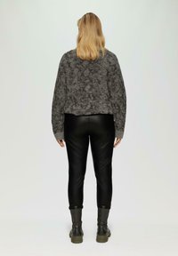 Grijze, gestructureerde trui gecombineerd met zwarte nep leren leggings en grijze enkelboots. De outfit heeft een ontspannen ontwerp met een casual pasvorm.