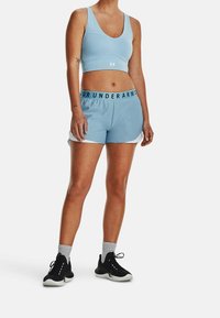Ljusblå sport-BH som matchas med kortbyxor med svart elastisk midja. Modellen bär svarta sneakers med grå ankelstrumpor.