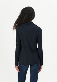 Navy ribbed knit sweater with a shawl collar, long sleeves, and a relaxed fit, paired with dark blue jeans.