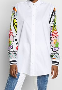 Witte overhem shirt met kleurrijke, gestreepte lange mouwen. Heeft strepen op de manchetten en opvallende graphics in tinten van groen, roze en oranje.