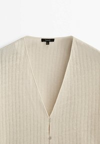 Beige geribde cardigan met een diepe V-hals, voorzien van een knoopsluiting aan de voorkant en een zachte, gestructureerde gebreide stof.