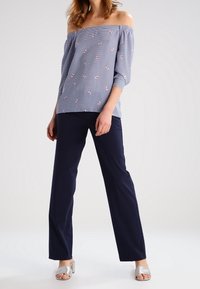 Pruhovaný top bez ramínek v modré a bílé barvě s růžovou květinovou výšivkou, spárovaný s námořnickými kalhotami s širokými nohavicemi a stříbrnými skluznými sandály.