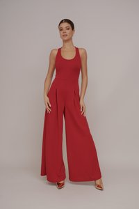 Combinaison sans manches rouge avec un corsage ajusté et des jambes larges plissées. Fabriquée à partir d'un tissu lisse, présentant un design simple sans motifs visibles.
