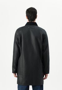 Black waterproof coat with a long straight silhouette, featuring a collar and back label. Smooth texture and minimal detailing.