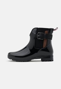 Bottines noires brillantes avec une accentuation de boucle, panneaux latéraux élastiques et une semelle texturée pour l'adhérence. Comprend une section contrastante marron.